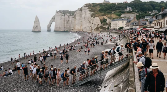 Foule de visiteurs sur la plage et le sentier d'accès d'un site à falaises de Normandie un matin d'août.