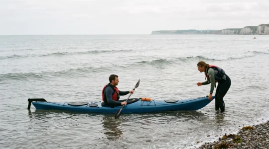 Un kayakiste débutant en combinaison reçoit les instructions d'un guide qui maintient son kayak de mer au bord de la côte normande.