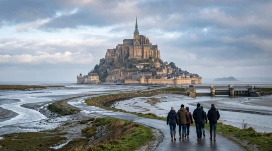 Vue large du Mont-Saint-Michel depuis la baie à marée basse, avec des visiteurs marchant vers l'abbaye sur le rocher