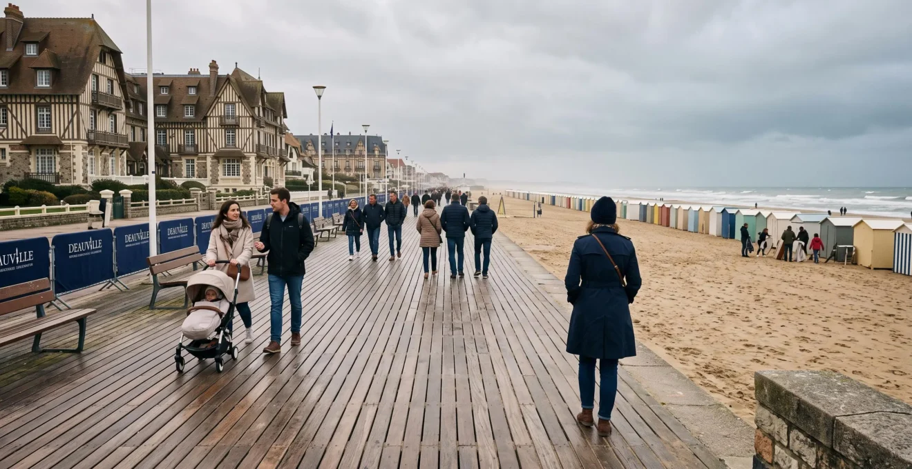 Passants marchant sur la promenade des Planches de Deauville un matin hors saison, avec la plage et les cabines de bain au loin.