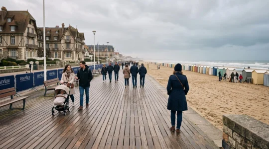 Passants marchant sur la promenade des Planches de Deauville un matin hors saison, avec la plage et les cabines de bain au loin.